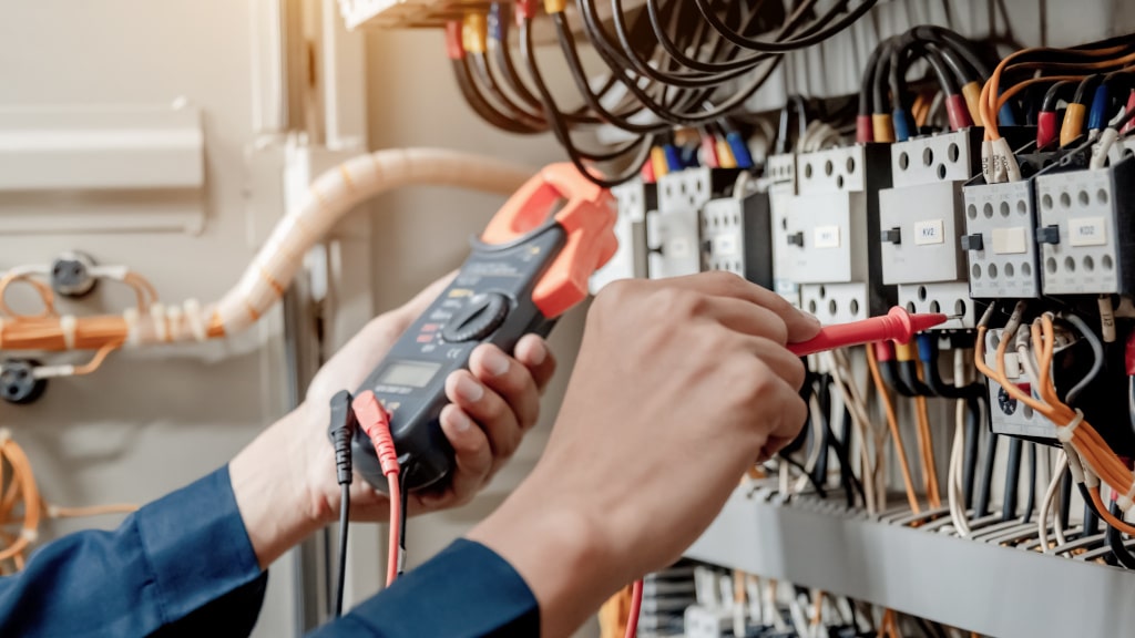 Elektrikeringeniør bruker et multimeter for å teste den elektriske installasjonen og strømledningen i et elektrisk systemkontrollskap.